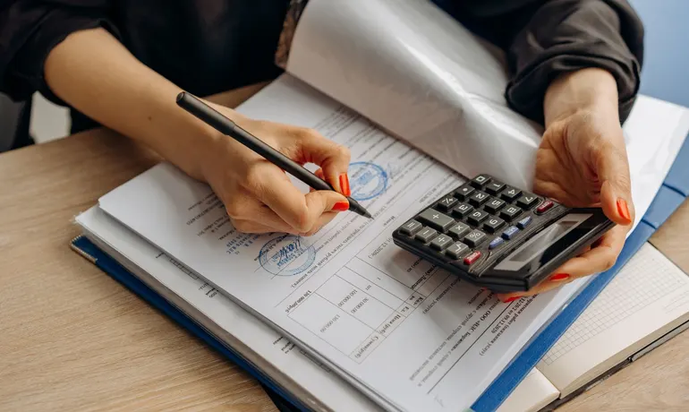 Pessoa preenchendo documentos com calculadora ao lado